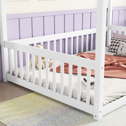 The Canopy Frame Floor Bed With Fence, Guardrails features white wooden rails and sits against a purple paneled wall. On the bed are a teddy bear, checkered pillows, and a pink blanket, with a soft rug placed on the floor nearby.