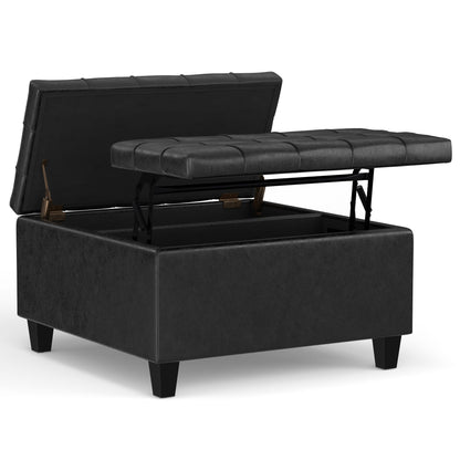 The Harrison - Large Coffee Table Storage Ottoman is shown open, displaying its storage space. It features black upholstery, a tufted hinged lid, and stands on four short legs.