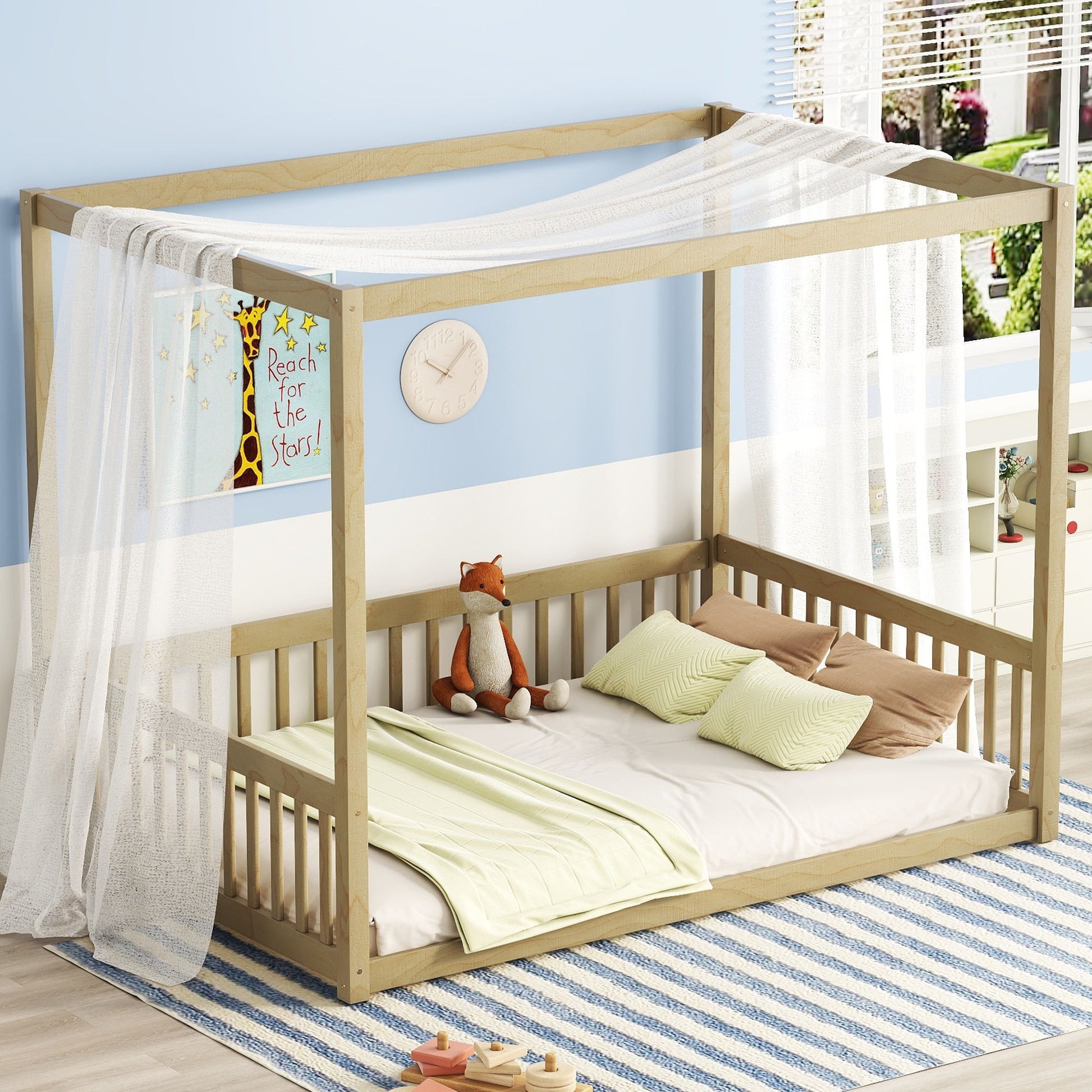 A Canopy Frame Floor Bed With Fence and guardrails features sheer white drapes, green bedding, a stuffed fox, and pillows atop a blue-striped rug in a bright room. A "Reach for the stars!" poster decorates the wall.