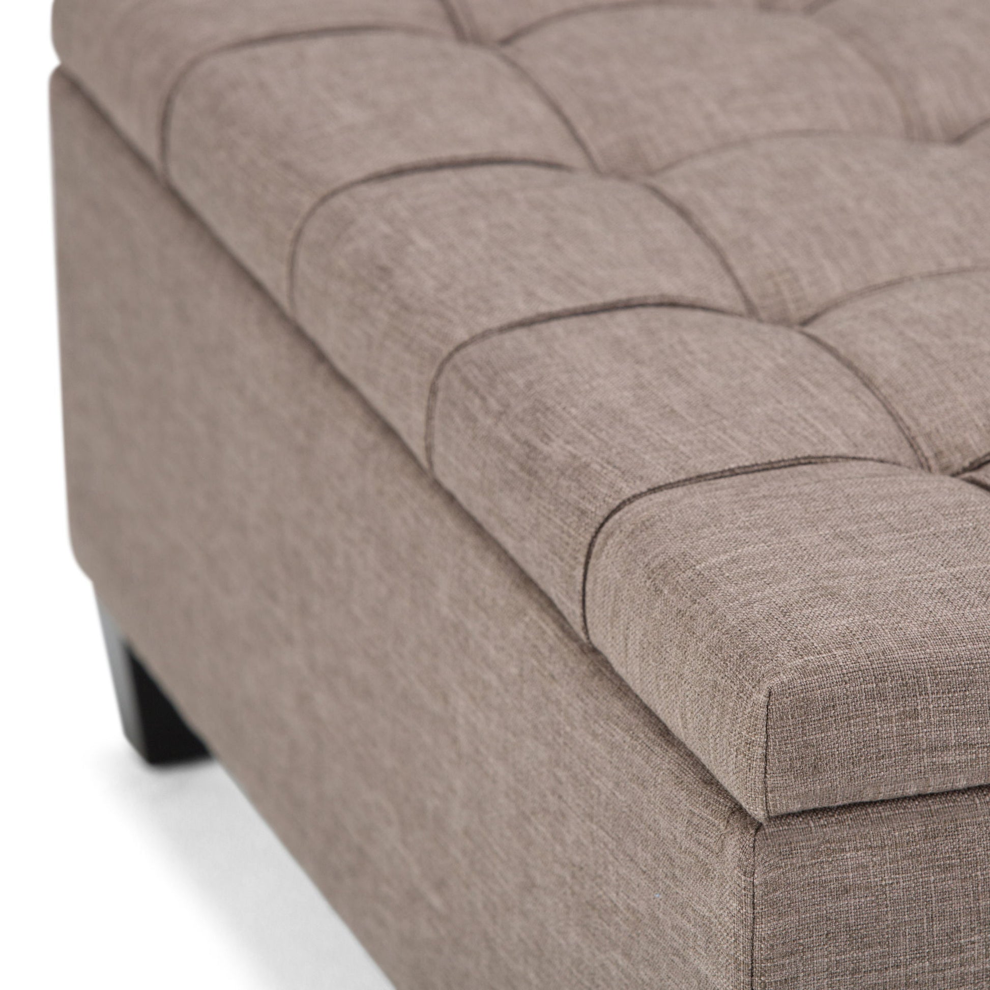 Close-up of the Harrison - Upholstered Coffee Table Storage Ottoman in beige, featuring a tufted square cushioned top and dark wood legs, shown against a white background.