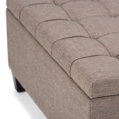 Close-up of the Harrison - Upholstered Coffee Table Storage Ottoman in beige, featuring a tufted square cushioned top and dark wood legs, shown against a white background.