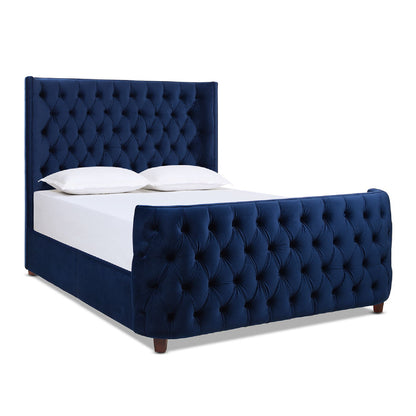 The Brooklyn Tufted Panel Bed features a tall navy blue velvet headboard and matching footboard, both with deep button detailing, and is styled with crisp white pillows and sheets.