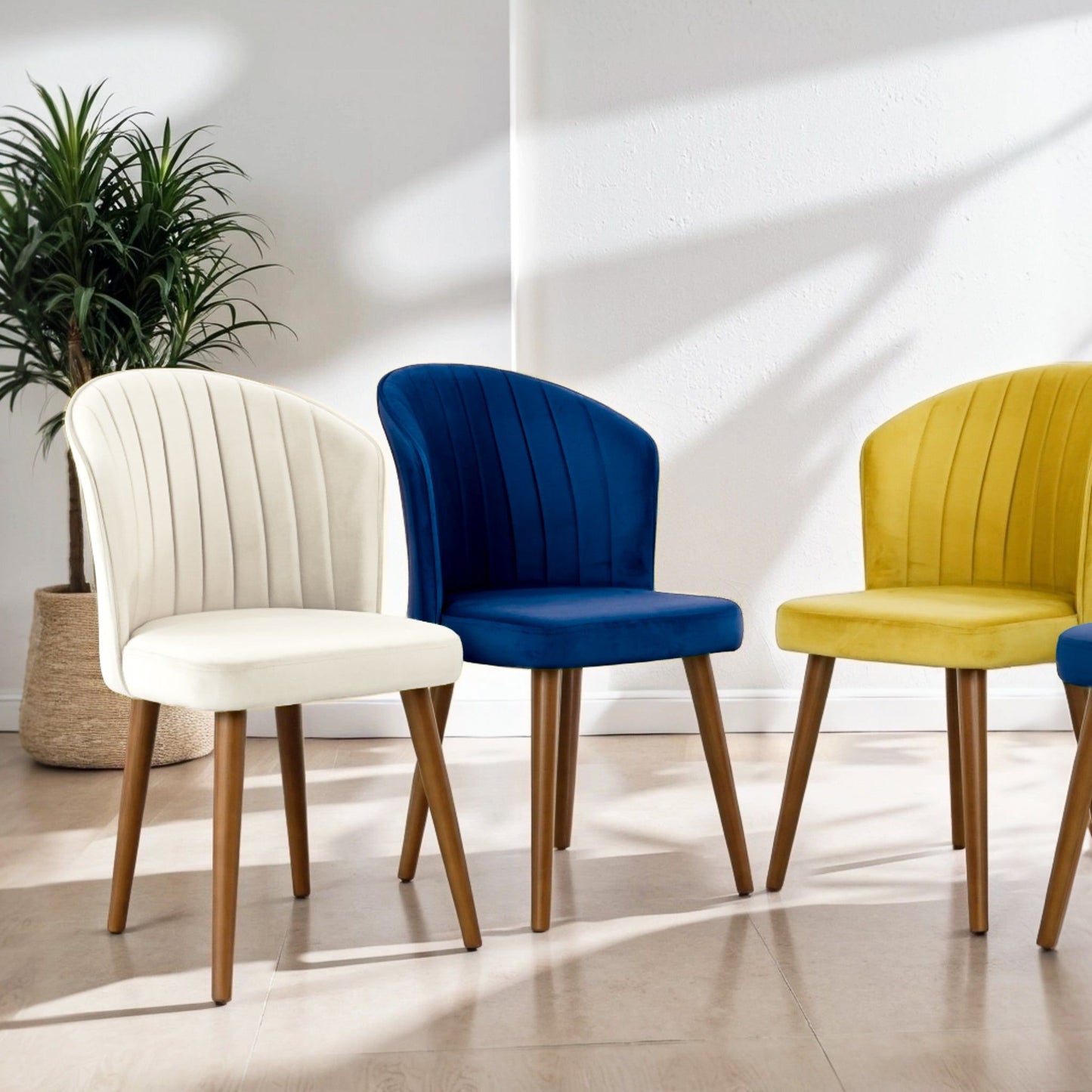 Two Parsons Comfortable Dining Chairs with wooden legs and velvet upholstery in cream, blue, and yellow are arranged in a sunlit room. A potted plant sits against a white wall, with shadows cast on the floor.