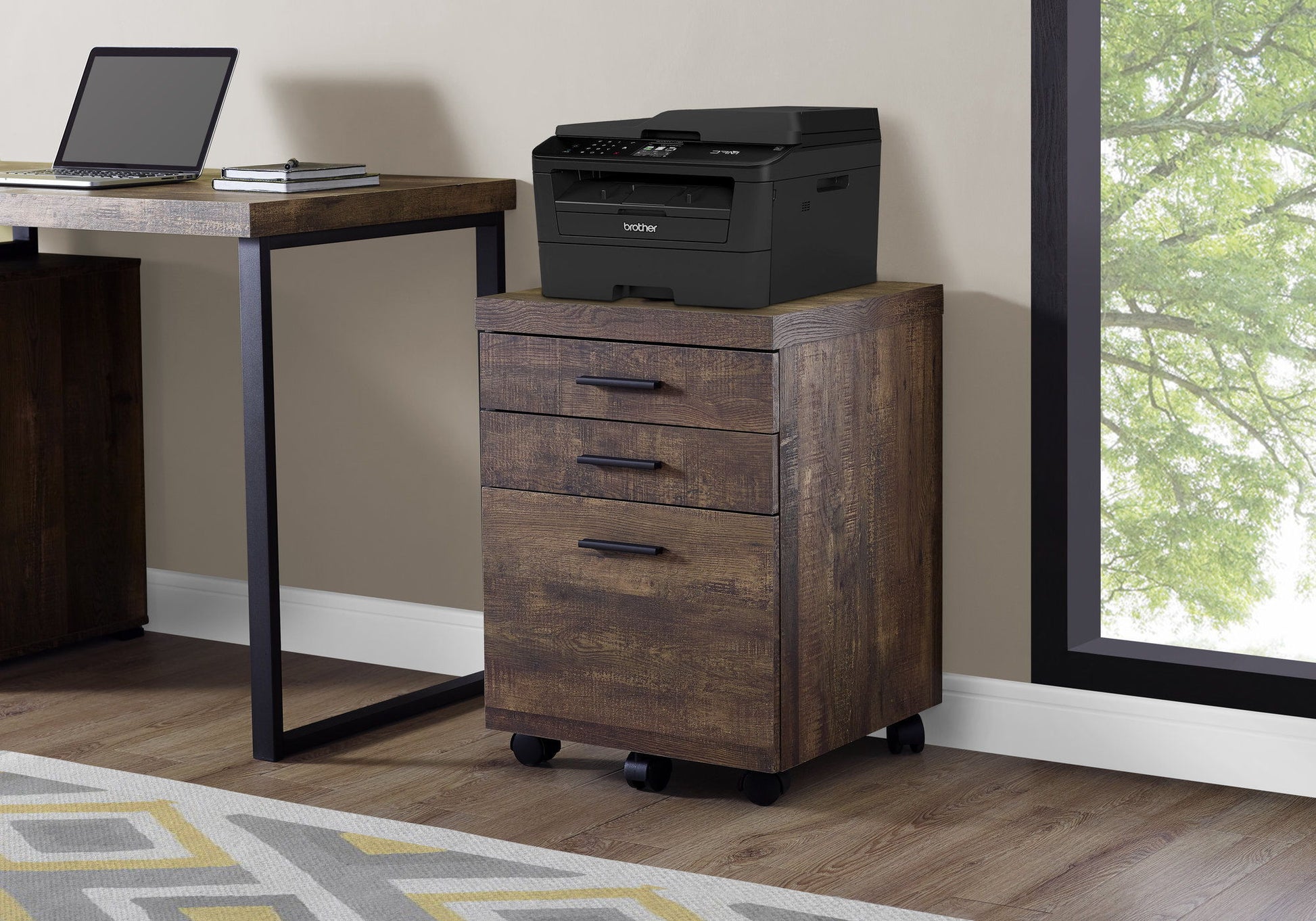 A File Cabinet Rolling Mobile Storage Drawers Printer Stand For Office with three drawers and black handles is on casters under a window, topped by a black printer beside a desk with a laptop. A geometric rug covers the floor.