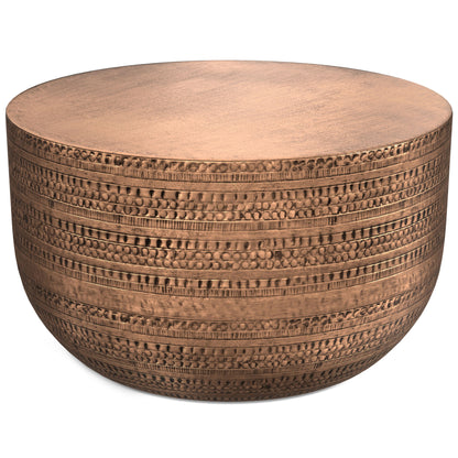 The Johnsen Handcrafted Metal Coffee Table features a round, copper-colored design with a hammered texture and decorative horizontal patterns around its curved sides.