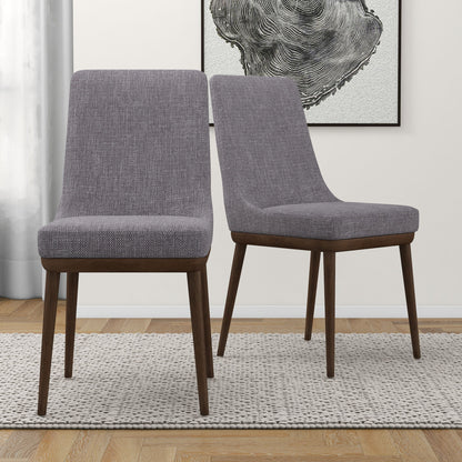 The Kate Mid-Century Modern Dining Chairs (Set of 2), featuring gray upholstery and dark wood legs, sit on a textured rug in a light-walled room with framed abstract art in the background.