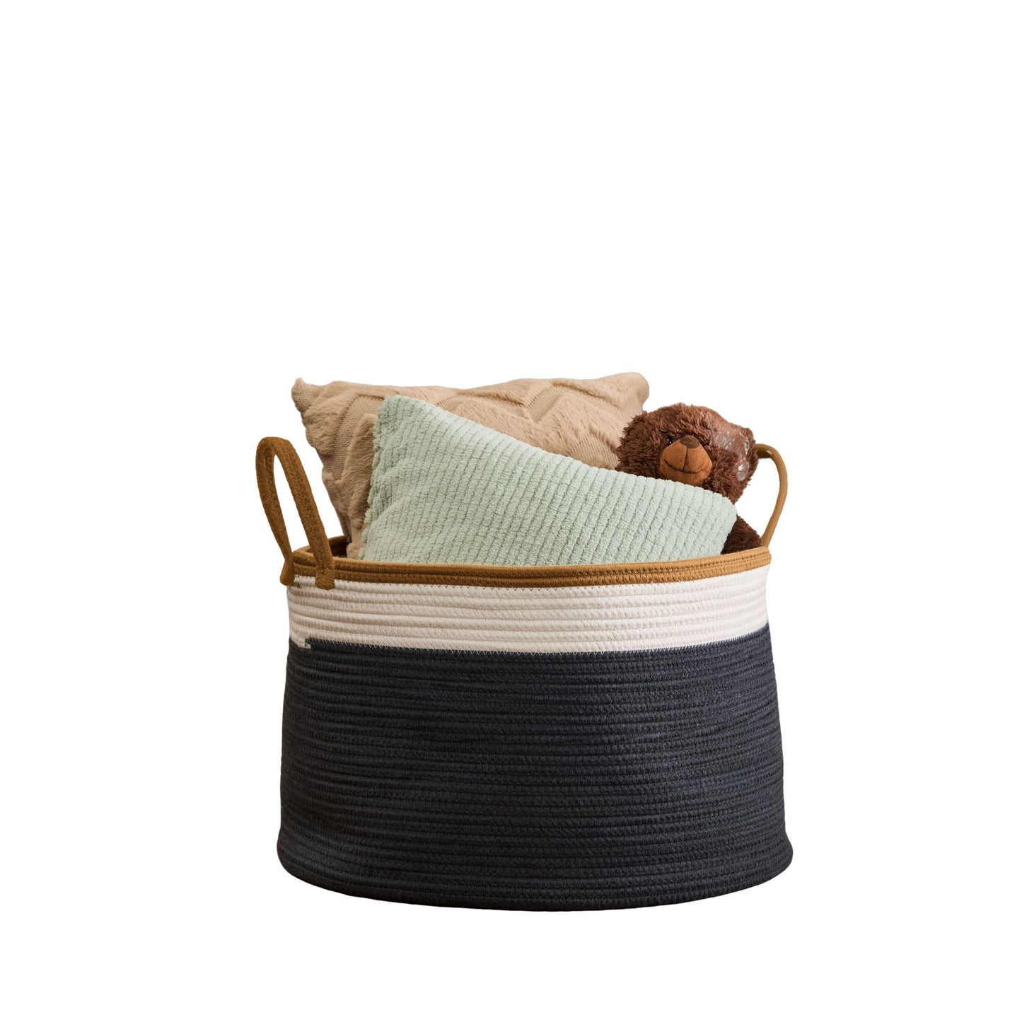 The Francis - Cotton Round Laundry and Storage Basket with tan handles holds a beige pillow, a light green pillow, and a brown teddy bear, all set against a plain white background.