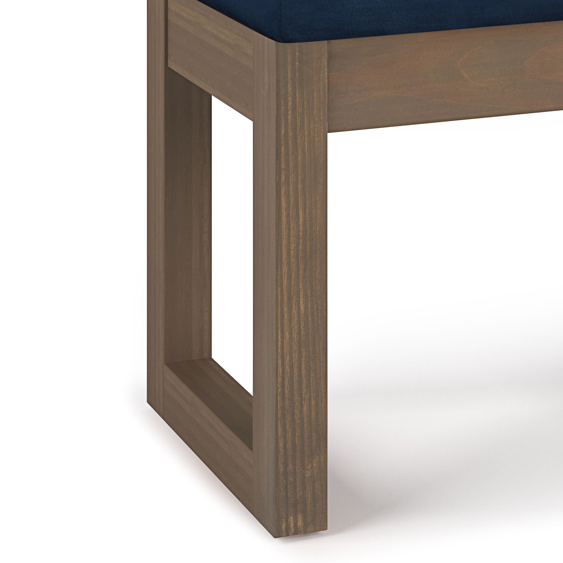 Close-up of the Milltown - Upholstered Ottoman Bench's wooden leg, featuring a rectangular open-frame design; the seat is upholstered in dark blue fabric. The background is plain white.