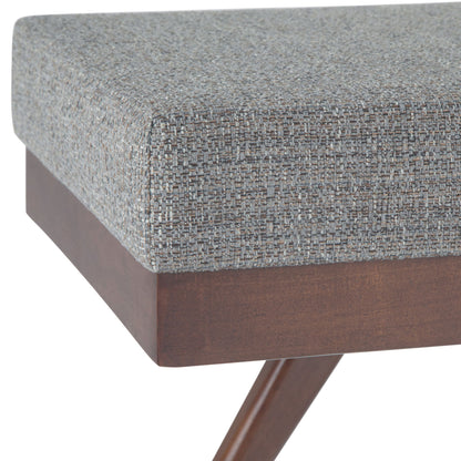 Close-up of the Chanelle Mid-Century Ottoman Bench featuring a cushioned seat in textured gray fabric and a wooden base with angled legs.