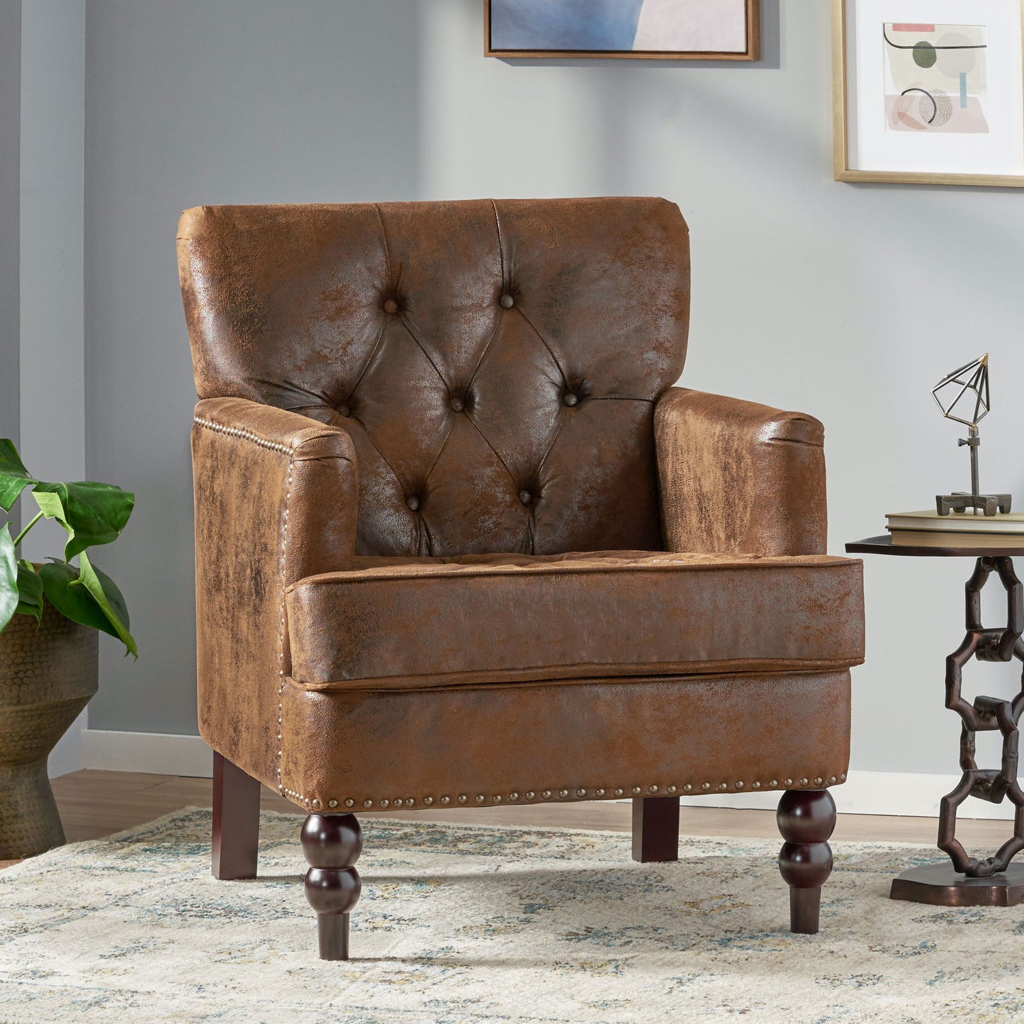 The Vitality Club Chair, featuring button tufted diamond stitching and turned legs, sits in a modern living room with light walls, framed art, a plant, and a side table.