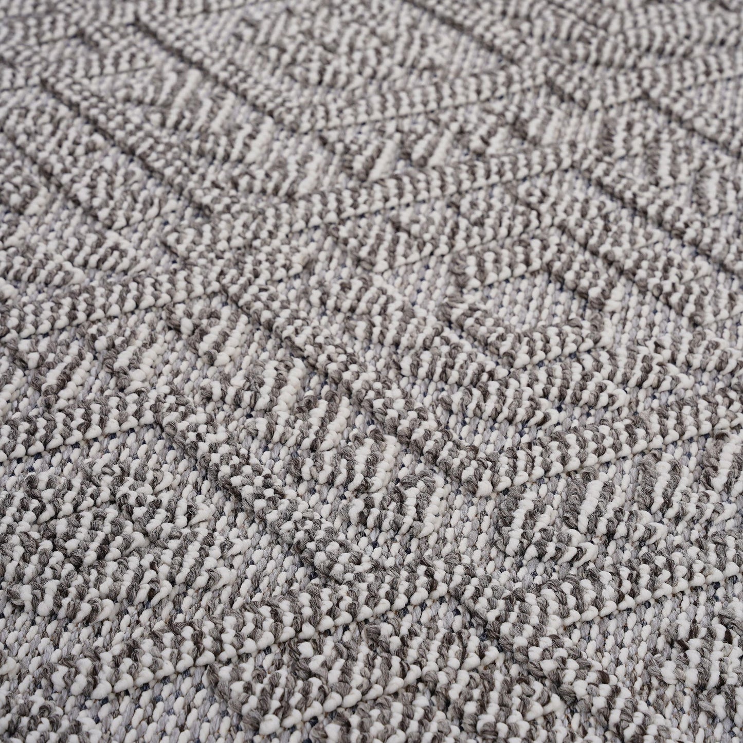 Close-up of the Guros - Traditional Indoor / Outdoor Area Rug, featuring a textured woven fabric with a geometric diamond pattern in shades of gray and off-white. Raised threads add a soft, three-dimensional effect to the surface.