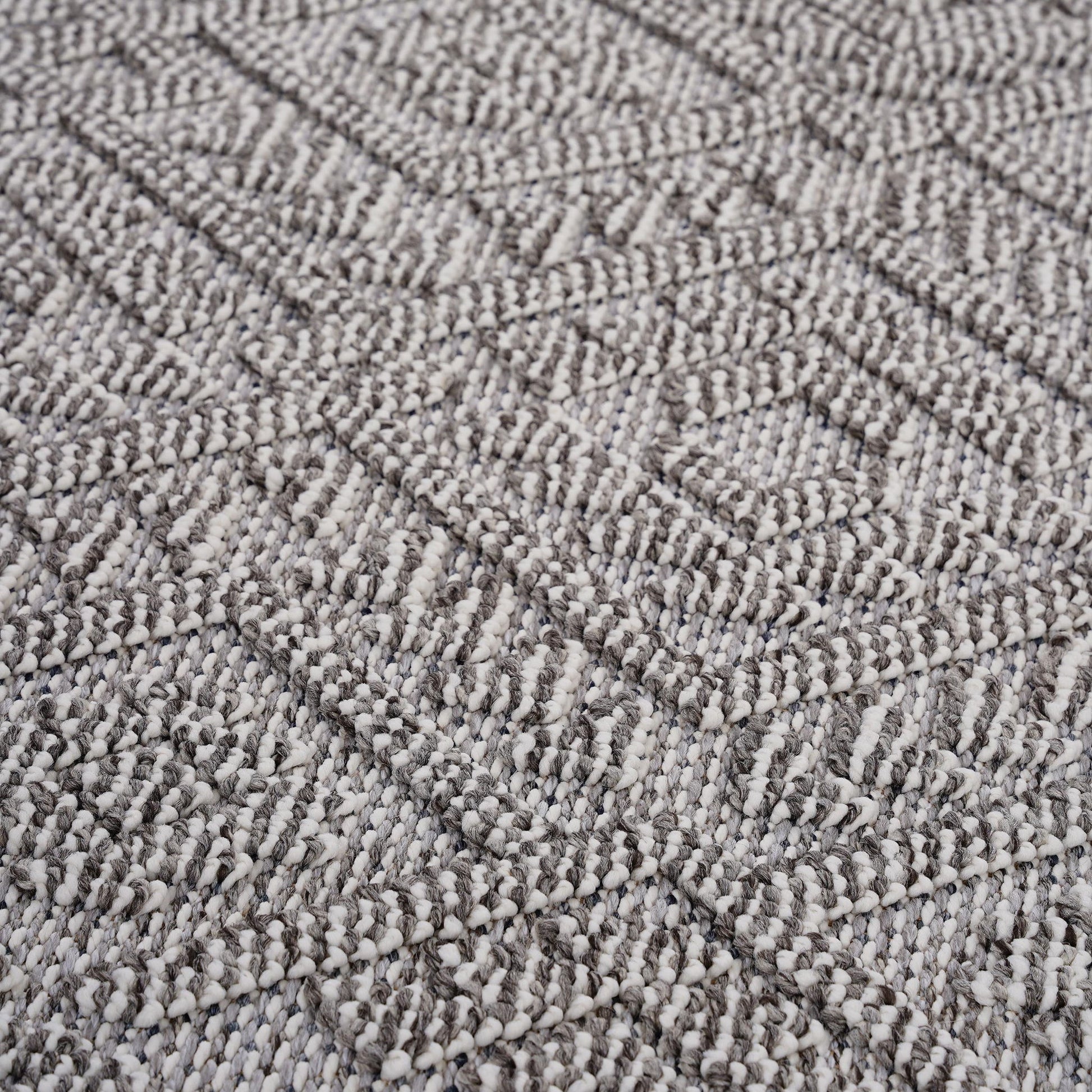 Close-up of the Guros - Traditional Indoor / Outdoor Area Rug, featuring a textured woven fabric with a geometric diamond pattern in shades of gray and off-white. Raised threads add a soft, three-dimensional effect to the surface.