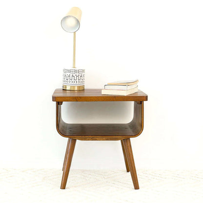 The Alice - Mid-Century Modern Table features angled legs and is styled with a table lamp, a decorative jar, and two stacked books on top, all set against a white background.