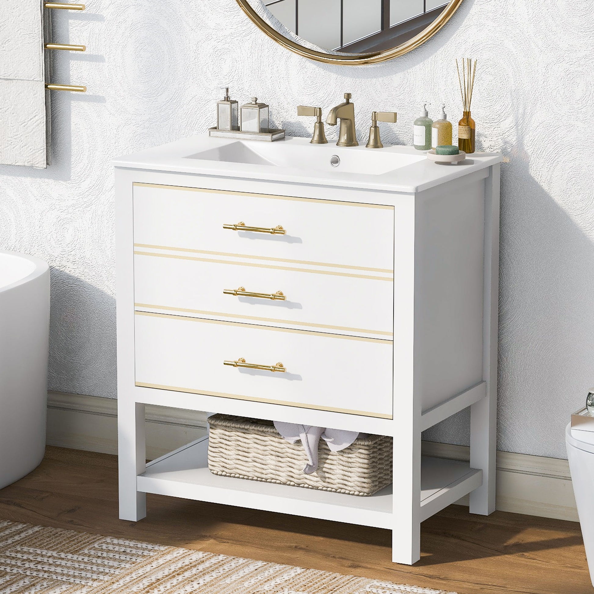 A Modern Bathroom Vanity Cabinet with open storage and two drawers, featuring white finish, gold handles, a sink with toiletries on top, a wicker basket on the lower shelf, and a round mirror partially visible above.