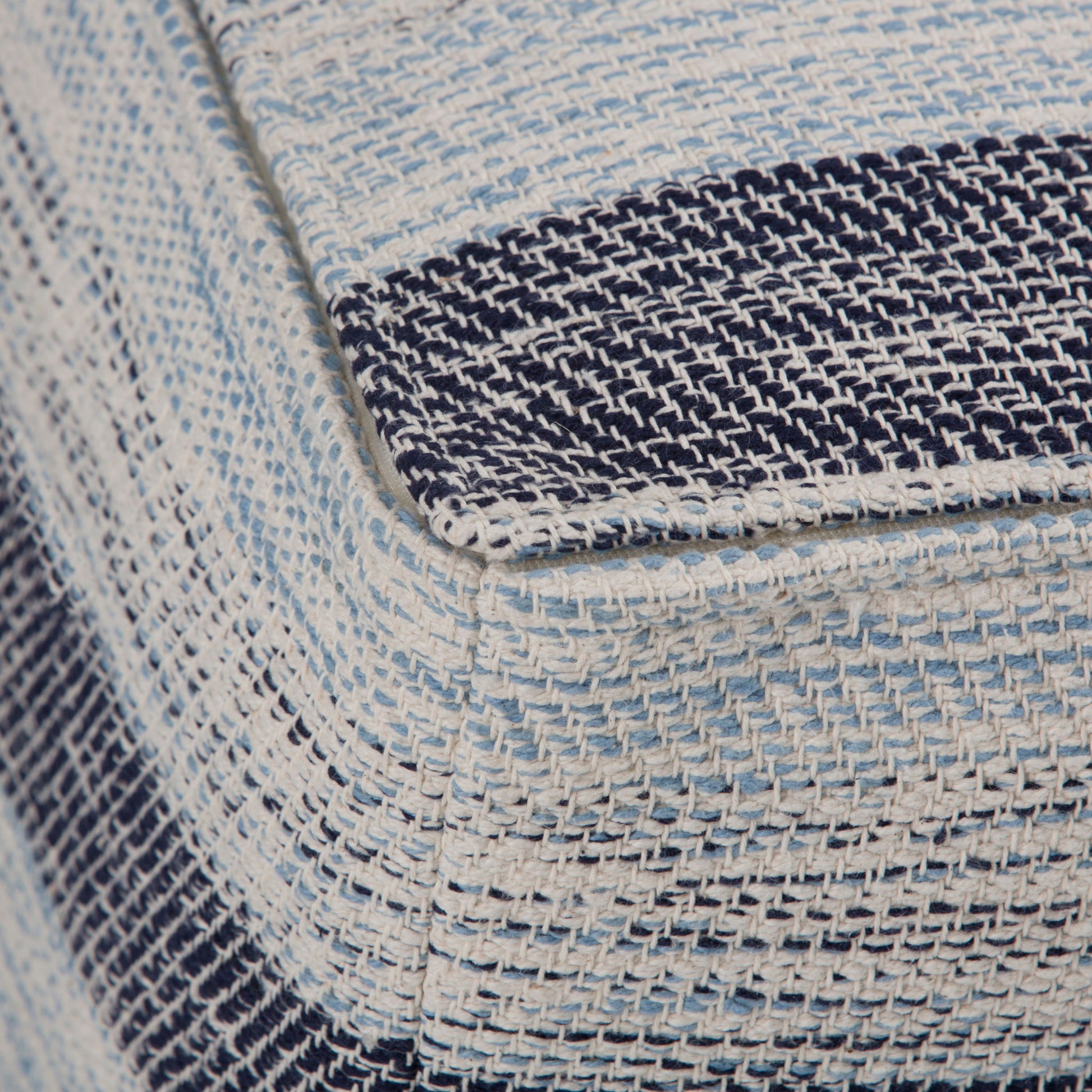Close-up of the Clay Square Pouf, Upholstered, showing its textured fabric corner with woven blue, navy, and white stripes.