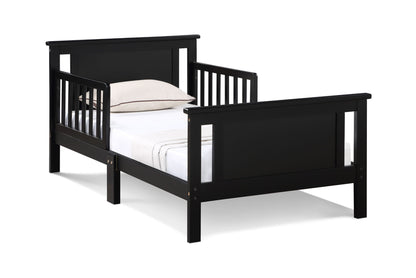 The Connelly - Reversible Panel Toddler Bed, shown in black wood with slatted sides and ends, is made up with a white sheet and light pillow on a white background.