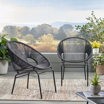 Two Nusa - Modern Chair Outdoor Seating pieces with circular woven designs sit on a patio rug, surrounded by potted plants. Trees and mountains create a scenic backdrop.
