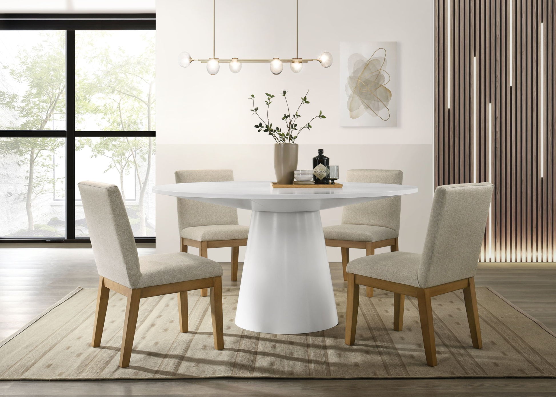 A modern dining room featuring the Jasper - Wide Contemporary Round Dining Table Set with four beige upholstered chairs, a central vase with greenery, abstract wall art, a linear pendant light, and sunlit large windows.