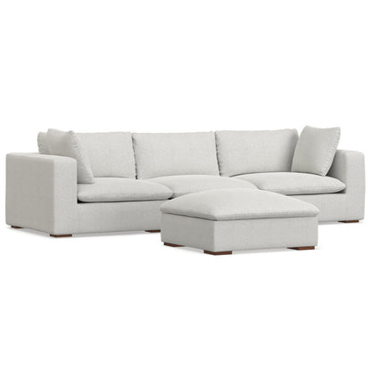 The Jasmine - Handcrafted Sofa And Ottoman features a modern light gray sectional with three seat cushions, three back cushions, two matching pillows, and a large rectangular ottoman, shown against a white background.