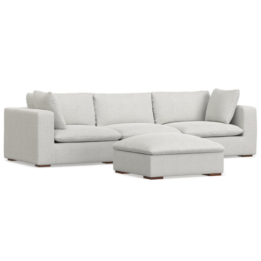 The Jasmine - Handcrafted Sofa And Ottoman features a modern light gray sectional with three seat cushions, three back cushions, two matching pillows, and a large rectangular ottoman, shown against a white background.