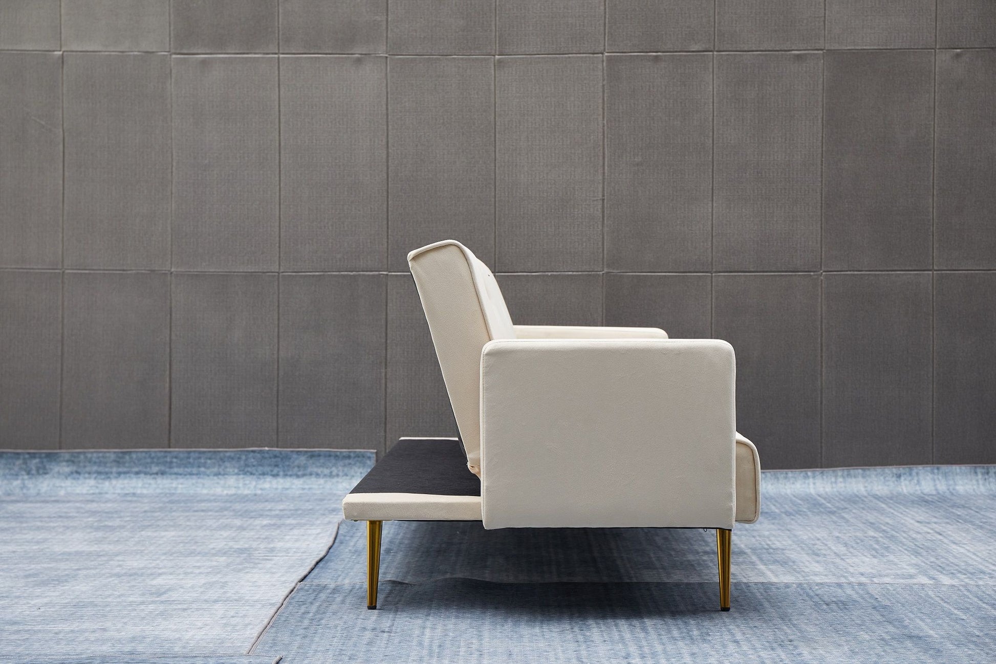The Comfort Compact Design Sofa Bed in modern white with gold legs is placed on a blue rug before a textured gray wall, creating a minimalistic and uncluttered setting.