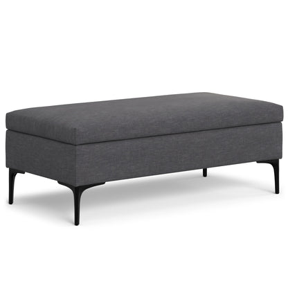 The Rebecca is a rectangular, dark gray upholstered storage ottoman with a cushioned top, slim black metal legs, and a lift-up lid for multifunctional use as a coffee table.