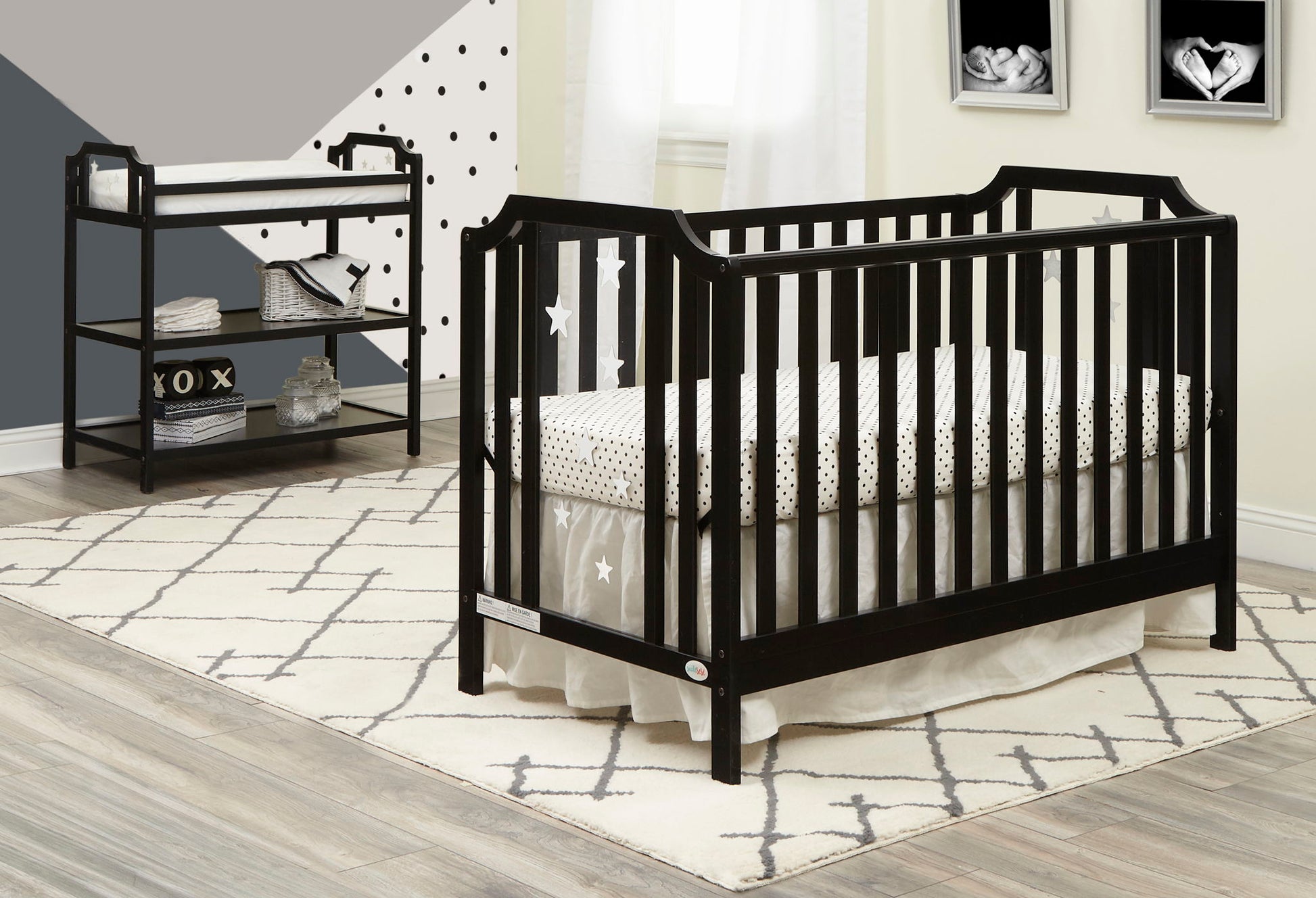 Modern nursery with a black crib, star and polka dot bedding, the Celeste Changing Table with shelves, geometric wall art, and a cream patterned rug on light wood floors.