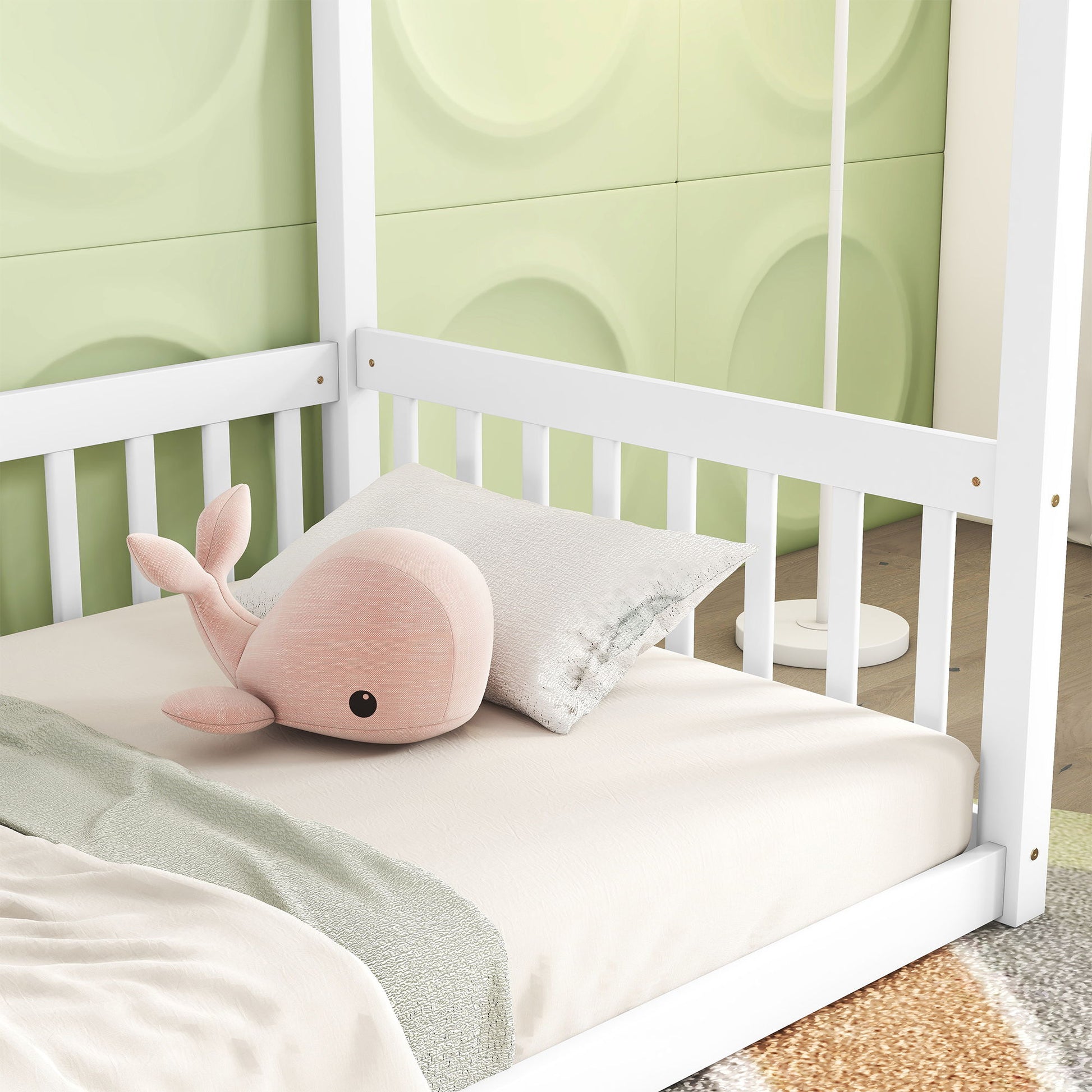 A soft pink whale plush rests on a light beige bed set inside a white Canopy Frame Floor Bed With Fence, Guardrails, against a green wall with circular patterns.