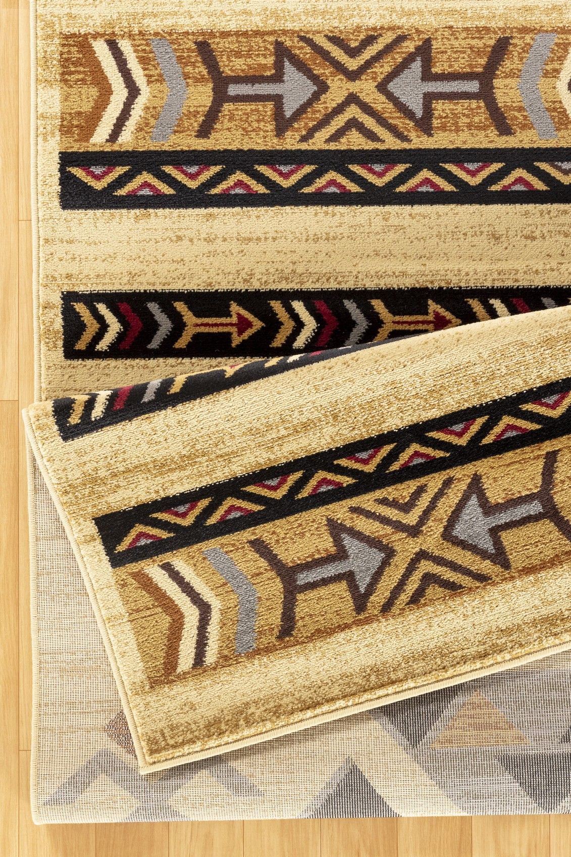 A close-up of two overlapping Tribes - GC_YLS4006 Southwest Area Rugs featuring geometric arrow patterns in brown, yellow, black, red, and gray on a light wood floor.