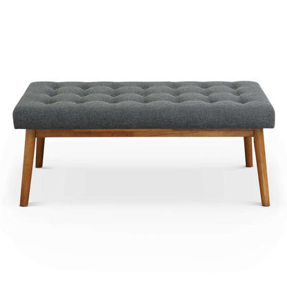 The Delilah Modern Bench features a tufted dark gray upholstered seat and four angled wooden legs, displayed against a plain white background.