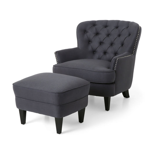 The Enchante Living Room Set features a dark gray tufted-back club chair with silver nailhead trim and dark wooden legs, paired with a matching rectangular ottoman, both displayed against a white background.