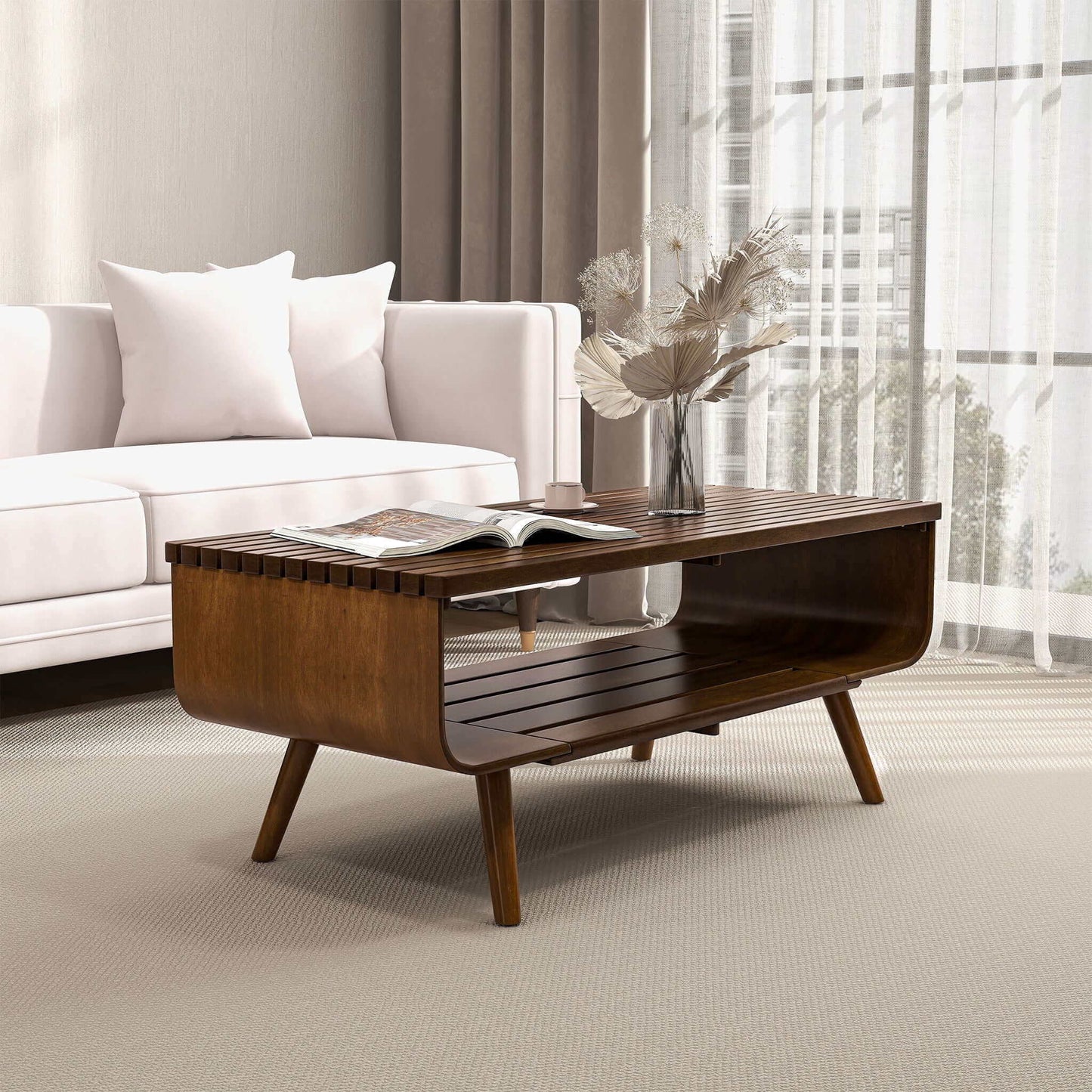 A modern living room featuring a white sofa, the Alice Mid-Century Modern Table with a book and vase of dried flowers, light curtains, and soft natural light streaming through a large window.