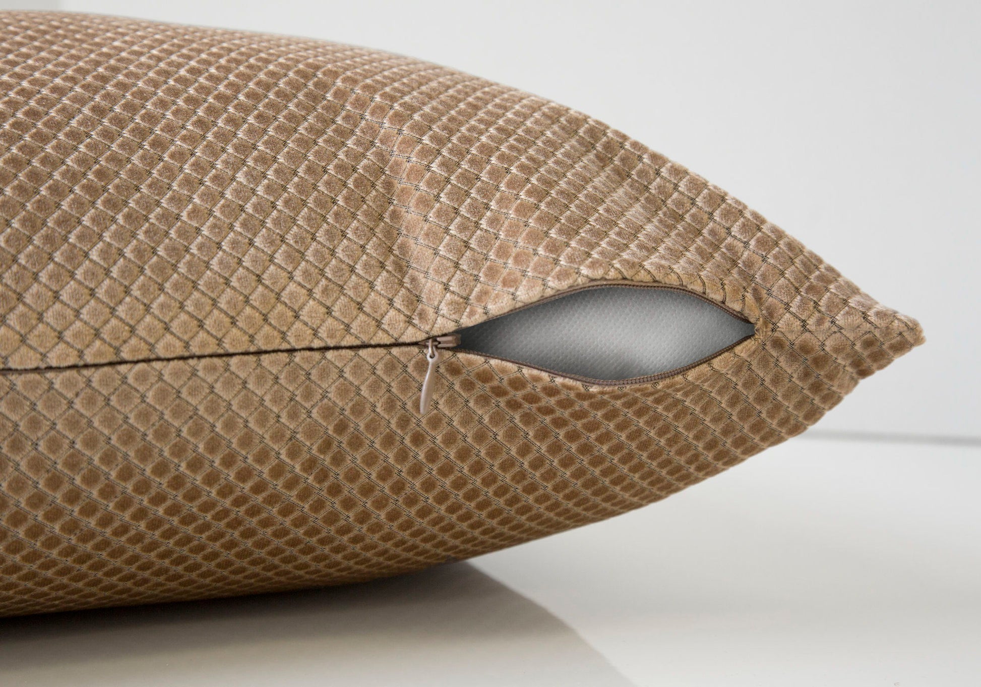 A close-up of the Pillow Square decorative throw shows its brown textured cover and a partially open zipper, exposing the white hypoallergenic insert. The background is light and plain.