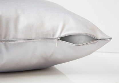 A close-up of a modern square decorative throw pillow in silver satin, insert included, with a partially open visible zipper revealing the hypoallergenic inner lining. The background is plain white.