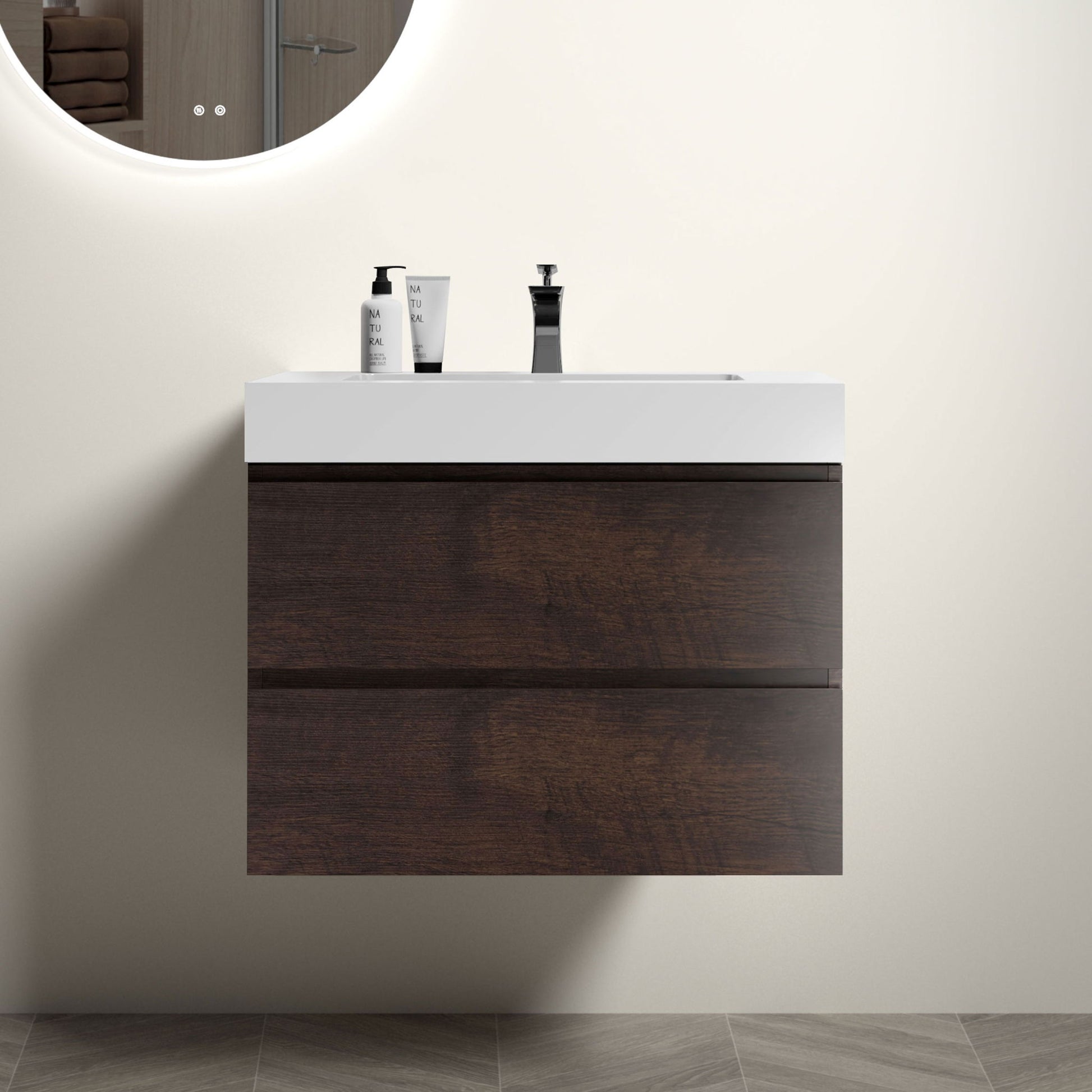 The Alice wall-mounted bathroom vanity with a one-piece white sink basin and large storage drawers sits against a light wall, topped by a round illuminated mirror, and set on gray geometric floor tiles.