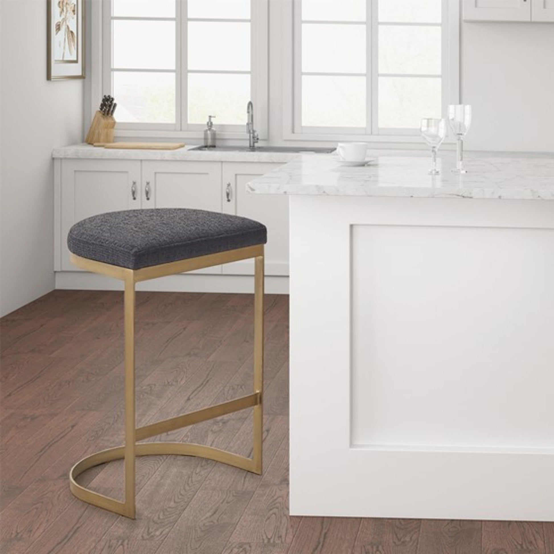 A modern kitchen with white cabinets, a marble island, two wine glasses, and a Counter Stool With Upholstered Seat, Metal Base - Charcoal / Antique Gold on a wooden floor.