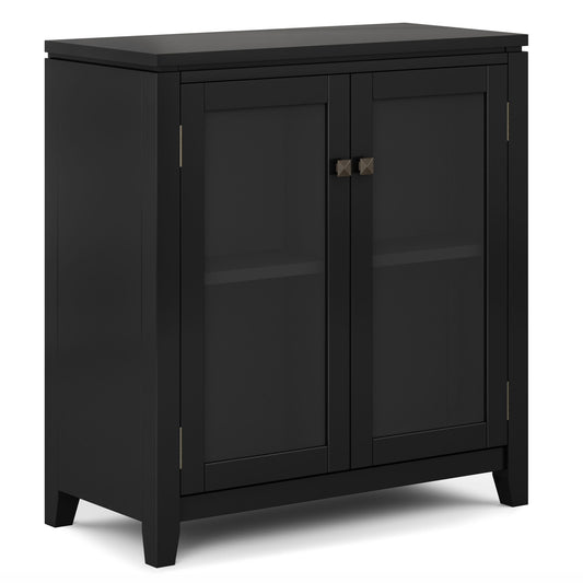 The Cosmopolitan Handcrafted Medium Storage Cabinet is a black wooden piece with two glass doors, each with a square metal handle. Its modern, straight-line design includes a visible lower shelf for extra storage.