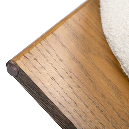 Close-up of the Bali - Round Upholstered Ottoman's wooden base, showcasing its smooth finish, rounded edge with a brown rubber cap, and partially visible textured cream-colored upholstery on the right.