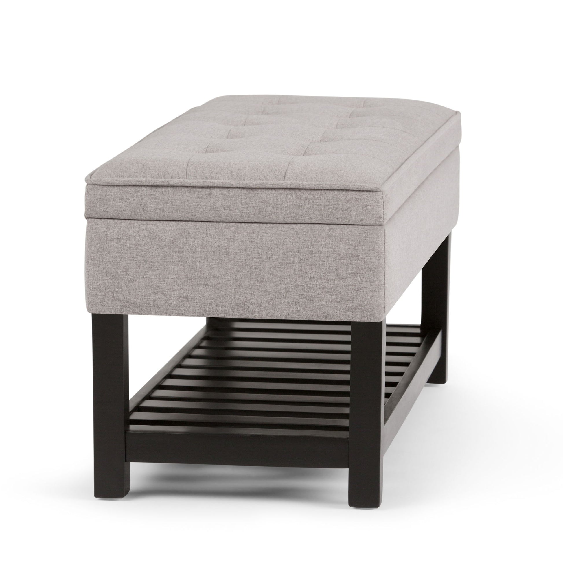 The Cosmopolitan Storage Ottoman Bench features a rectangular, light gray upholstered design with a tufted top, black wooden legs, and an open slatted shelf for extra storage.