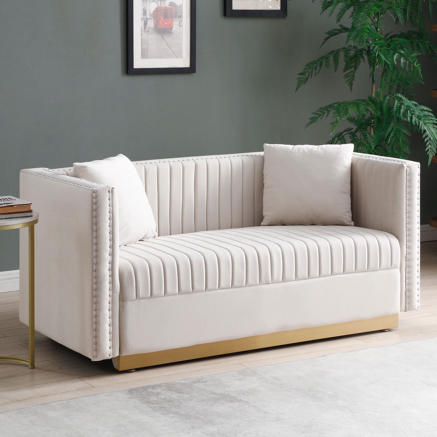 The Contemporary Vertical Channel Tufted Velvet Sofa Loveseat 2-Piece Set features cream upholstery, gold base, nailhead trim, and comes with four matching pillows. It's arranged near a round side table, potted plant, and framed art on a gray wall.