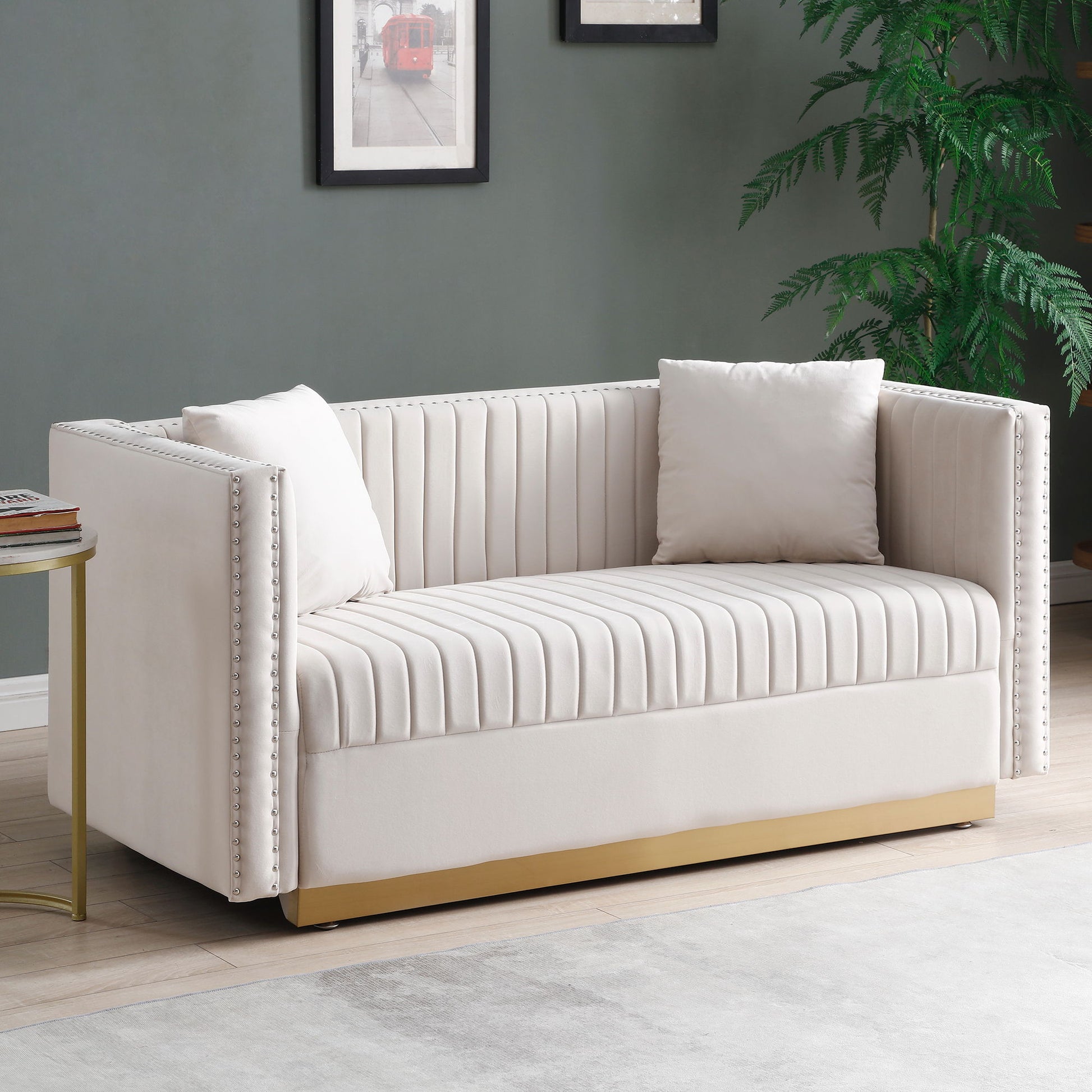 The Contemporary Vertical Channel Tufted Velvet Sofa Loveseat 2-Piece Set features cream upholstery, gold base, nailhead trim, and comes with four matching pillows. It's arranged near a round side table, potted plant, and framed art on a gray wall.