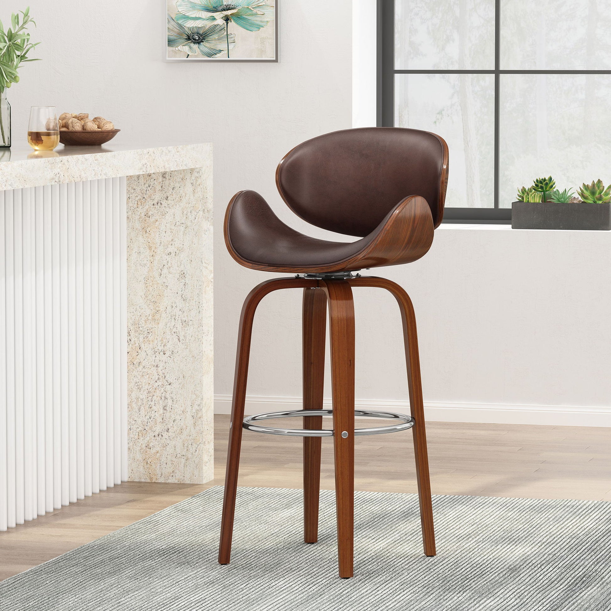 The Lumos Mid Century Modern Upholstered Swivel Barstool features a curved wooden frame, brown cushioned seat and backrest, and a metal footrest, shown on a gray rug in a bright room with a counter, wall art, and potted plants.