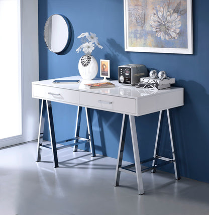 The Coleen High Gloss Writing Desk With USB, finished in white with chrome legs, stands against a blue wall and is styled with white flowers, books, a vintage radio, metallic accents, and topped by a round mirror and floral artwork.