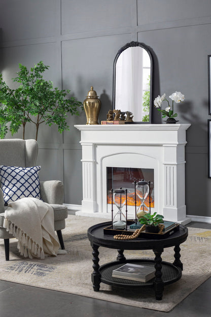 A modern living room features a white fireplace topped with the Hand Carved Rose Antique Mirror Frame, potted plants, a gold vase, gray armchair with blanket, and a round black coffee table on a beige rug.