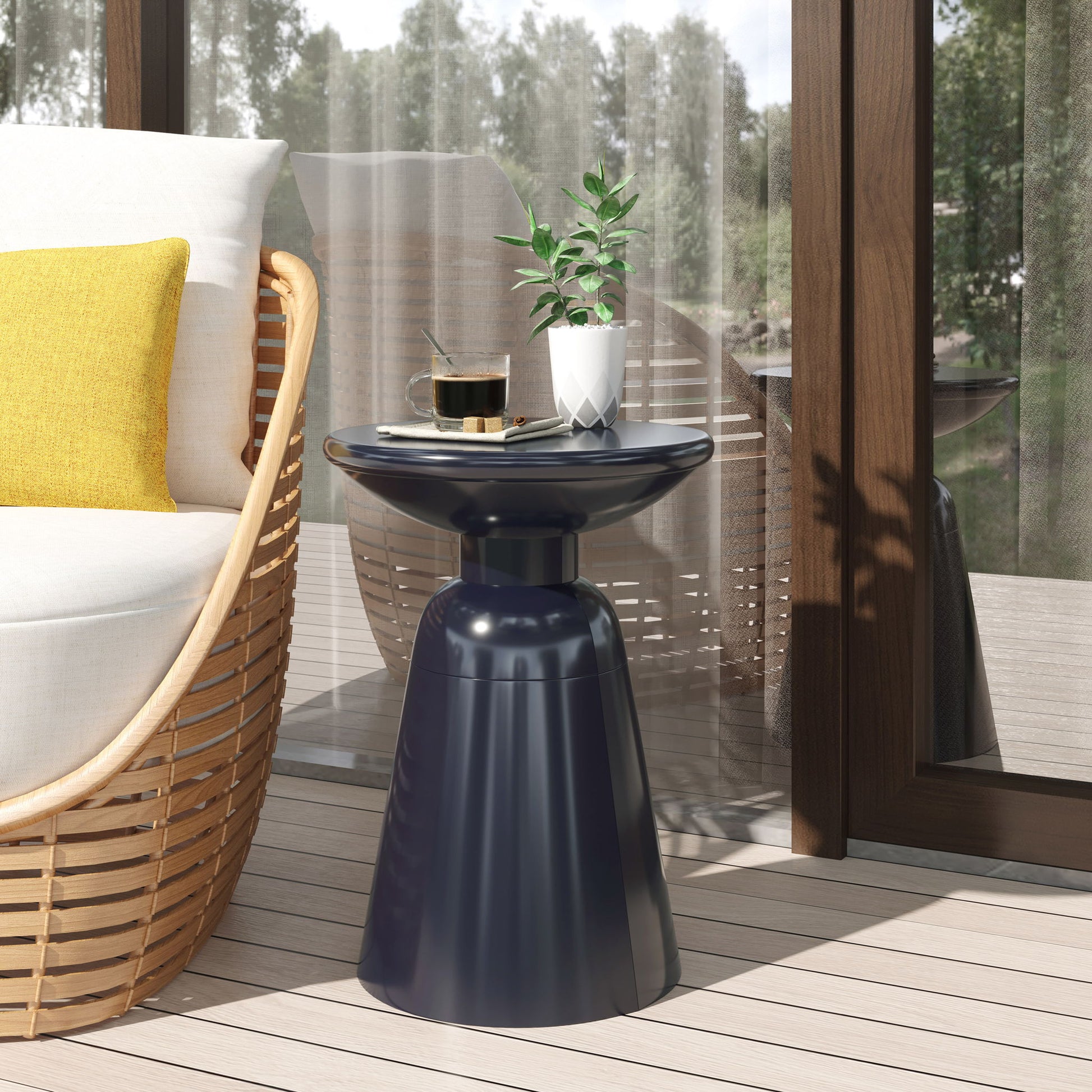 The Outdoor Modern Metal End Large Table, in navy blue, holds a potted plant, a glass of coffee, and a plate beside a cushioned rattan chair with a yellow pillow near a window with views of a wooden deck and greenery.