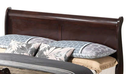 The Panel Sleigh Bed features a dark wood headboard, two blue geometric pillows, two floral pillows, beige sheets, and a dark gray blanket for a stylish and neatly made look.