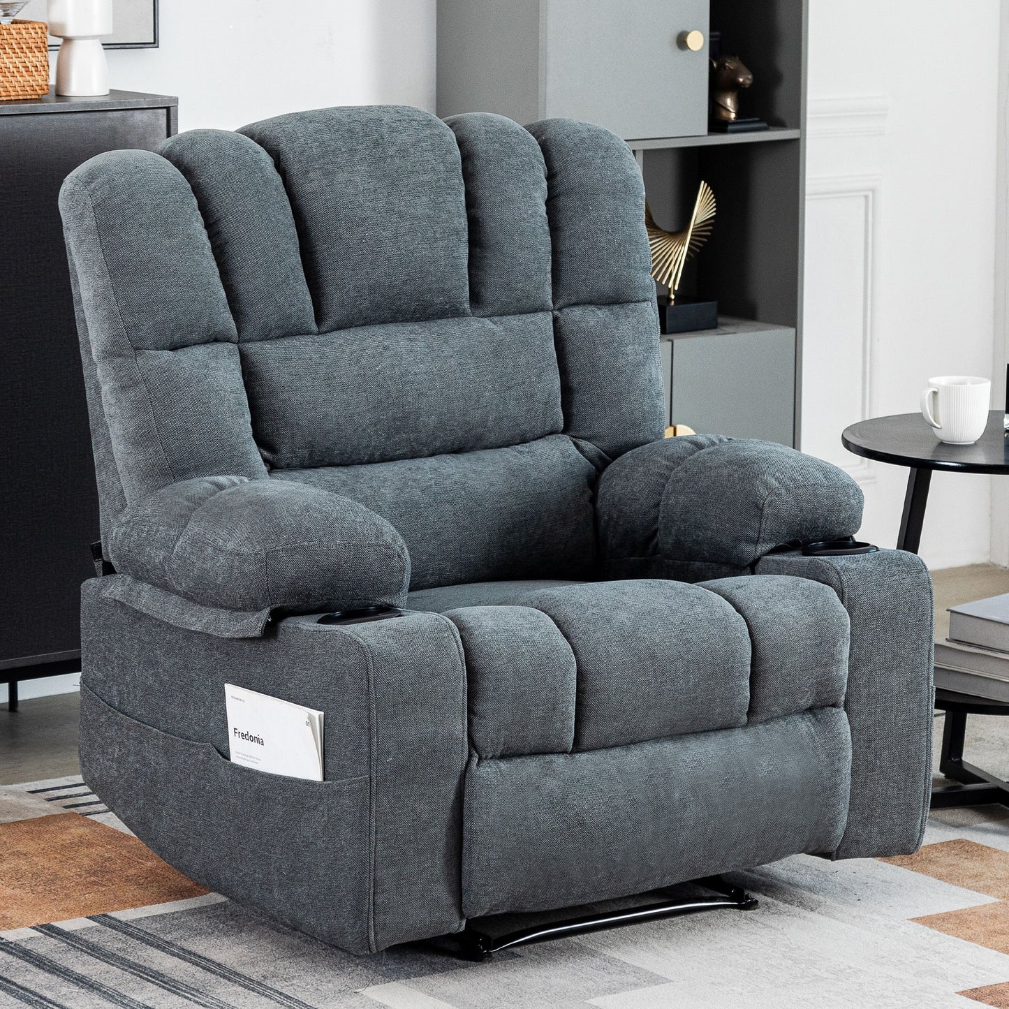 The Massage Recliner Chair Sofa With Heating Vibration, featuring plush gray upholstery and tufted cushions, is placed in a modern living room beside a small side table with a cup and a decorative cabinet in the background.