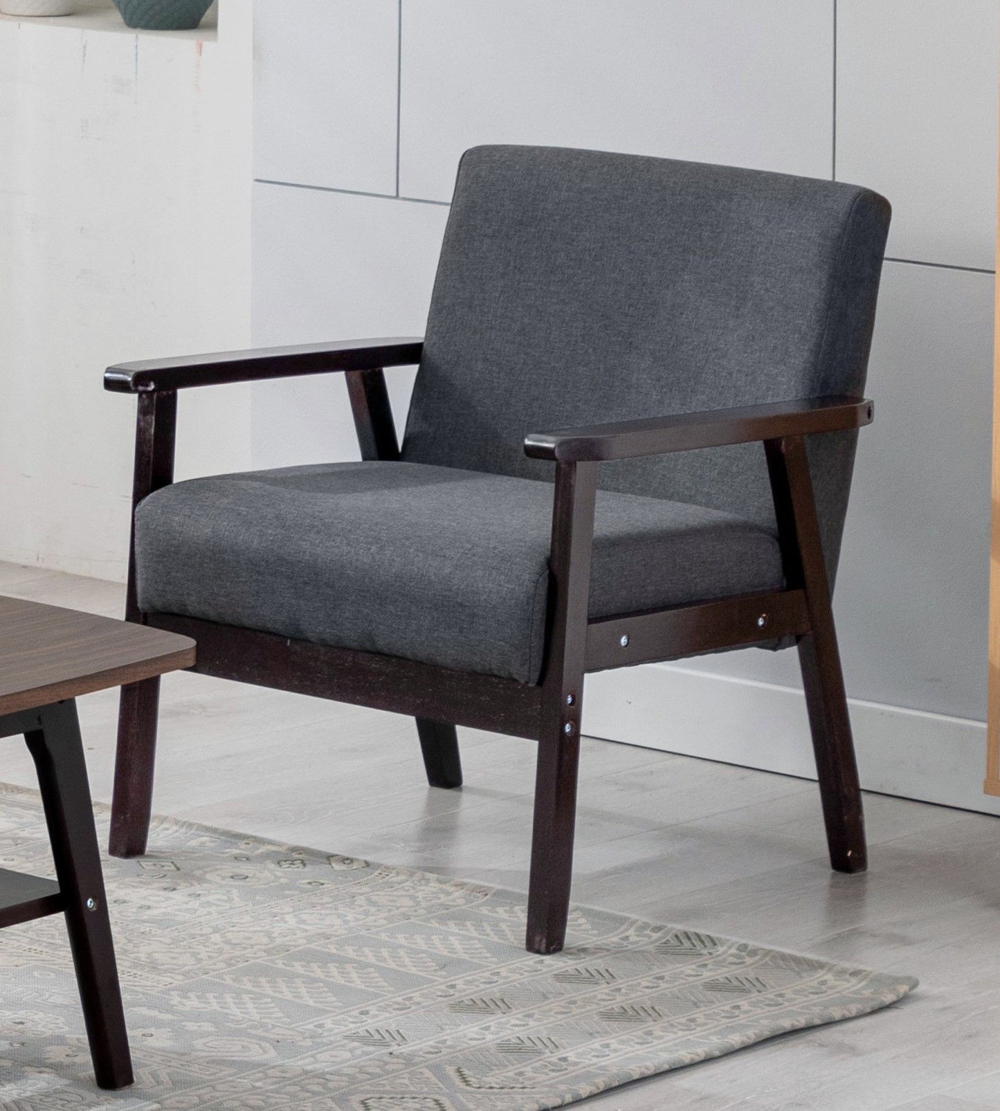 The Bahamas - Linen Fabric Chair, featuring a dark wooden frame and dark gray upholstery, sits on a light-patterned rug beside a wooden coffee table in a modern room.