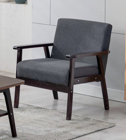 The Bahamas - Linen Fabric Chair, featuring a dark wooden frame and dark gray upholstery, sits on a light-patterned rug beside a wooden coffee table in a modern room.