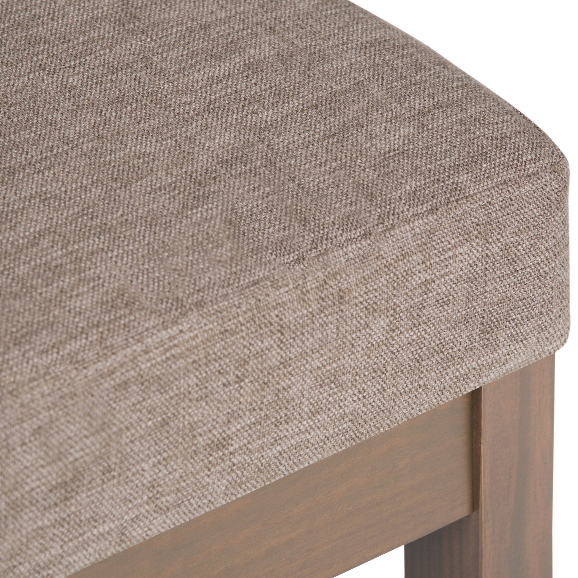 Close-up of the Milltown Upholstered Ottoman Bench featuring a cushioned seat with light brown textured fabric and a wooden frame.